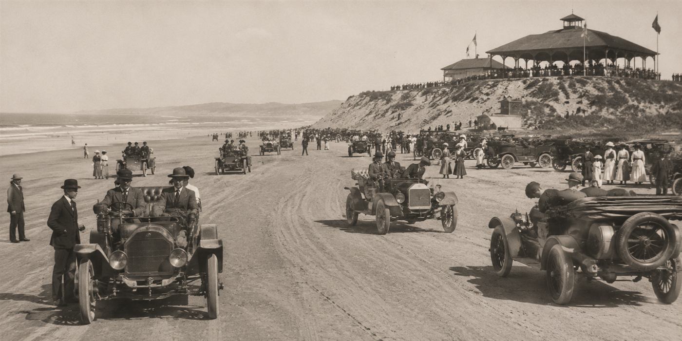 Early 1900s automobiles lined up on the beach at Pismo with the Pavilion Hill dance pavilion in the background