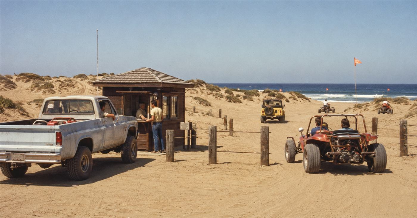 AI recreation of an early 1980s wooden entrance kiosk with a ranger checking in vehicles at Oceano Dunes