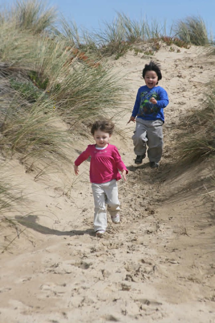 Two kids running down a sand dune