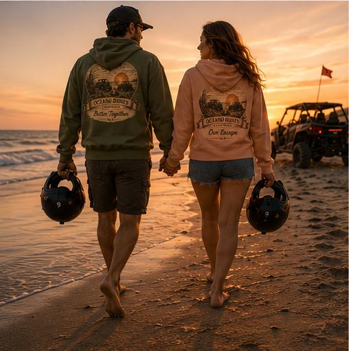 A couple walking the beach carrying helmets, wearing CCWheelers Sunset Collection crop hoodies at sunset, Oceano Dunes California