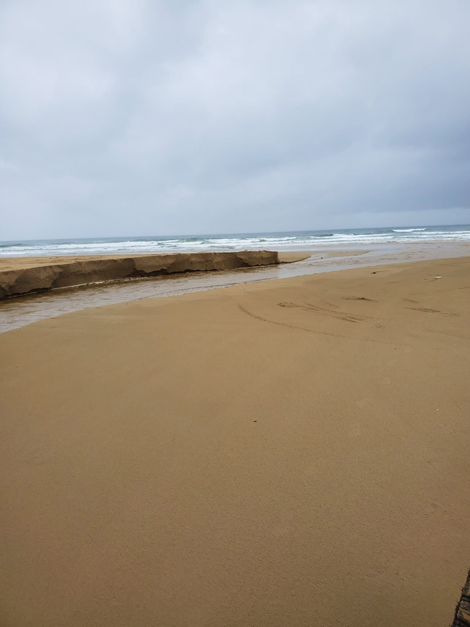 Eroded sand bank cut by Arroyo Grande Creek on an overcast day at Oceano Dunes
