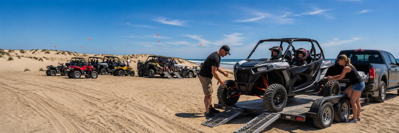A family loading a UTV off a trailer at the beach entrance for a day trip to Oceano Dunes