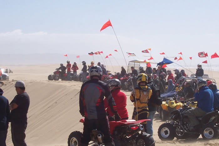 Group of quad riders with whip flags gathered on the dunes at Oceano Dunes, California