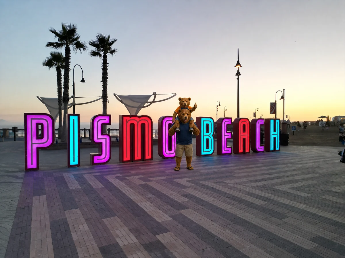 Oso carrying his son on his shoulders between the giant illuminated Pismo Beach letters